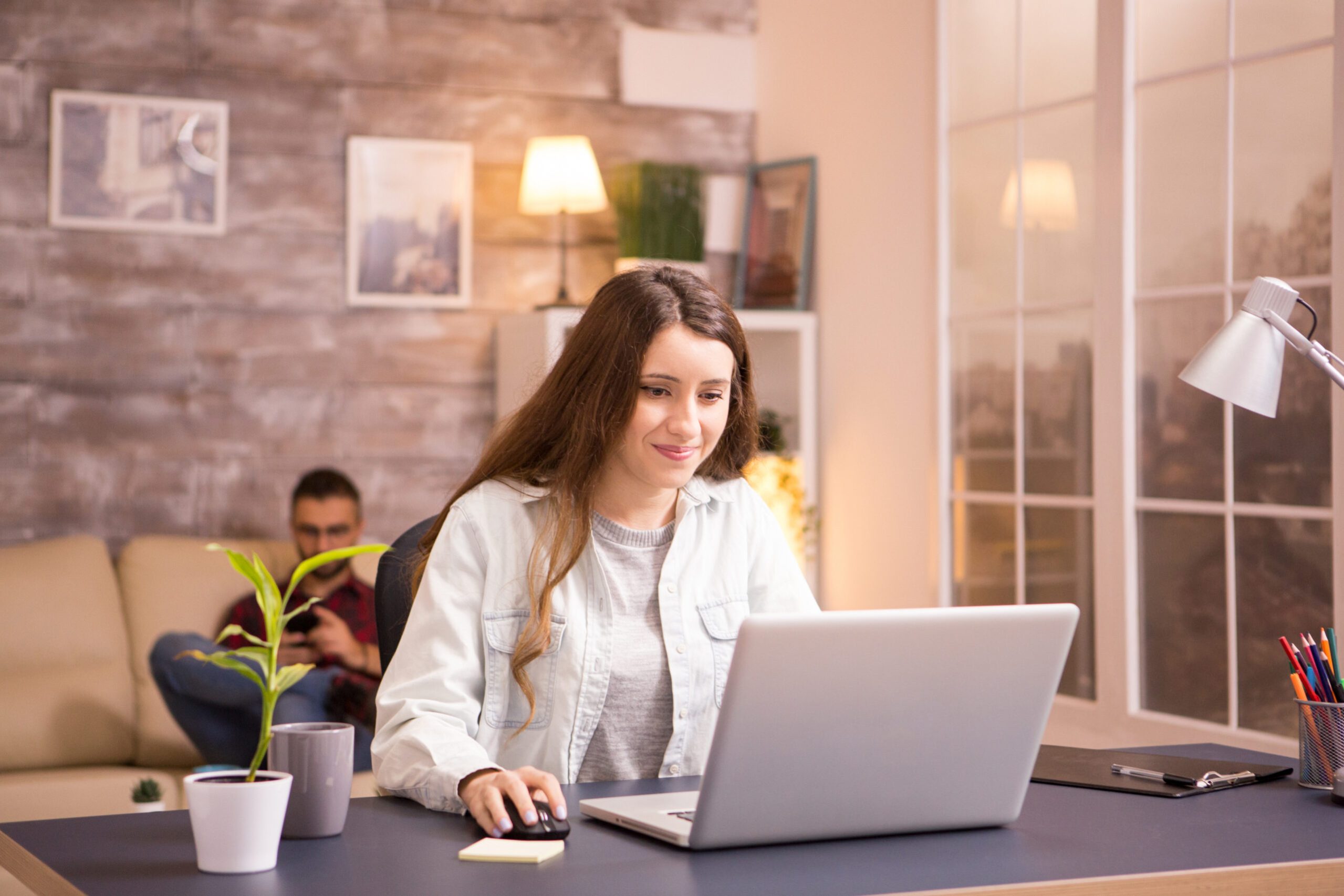 cheerful-young-woman-smiling-while-working-laptop-from-home-boyfriend-relaxing-sofa-background.jpg